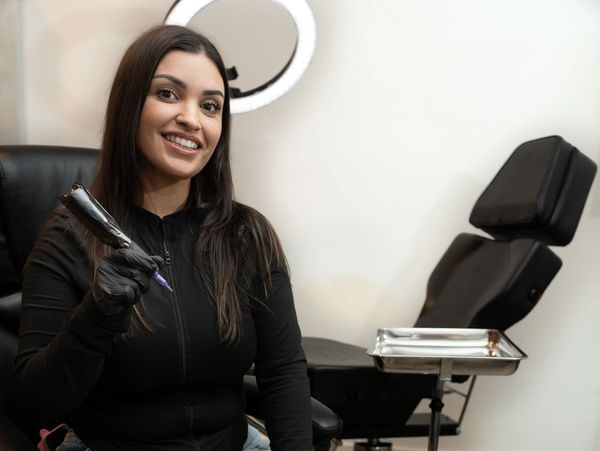 A smiling tattoo artist holding a tattoo machine in a studio.