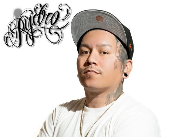 Man with tattoos and a cap posing confidently against a white background.