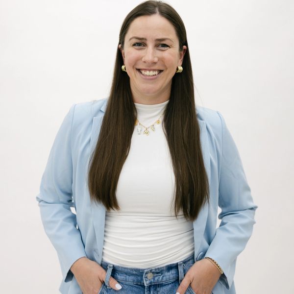 Smiling woman in a light blue blazer and jeans posing confidently.