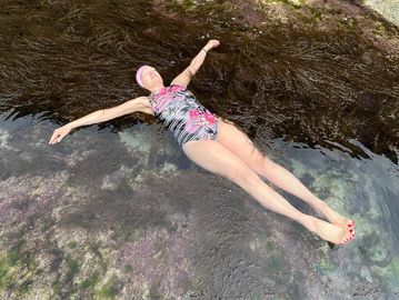 A woman floats peacefully on clear water near seaweed.