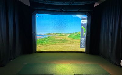 Indoor golf simulator setup with a digital course display.