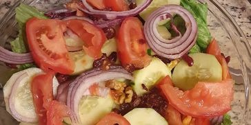 Fresh salad with tomatoes, cucumbers, red onions, walnuts, and lettuce.