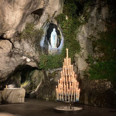 A statue of Virgin Mary in a cave with lit candles in front.