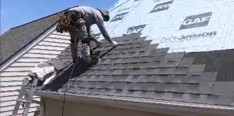 Worker installing asphalt shingles on a roof under sunny weather.