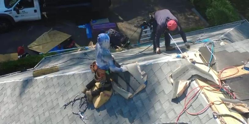 Two workers repairing a shingled roof on a sunny day.