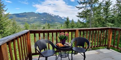 A cozy balcony with two chairs and a table overlooking mountains.