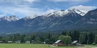 A picturesque mountain range with snow-capped peaks above a green valley and scattered houses.
