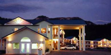 A warmly lit hotel exterior at dusk with cars parked outside.