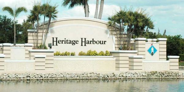 Entrance sign for Heritage Harbour surrounded by palm trees and water.