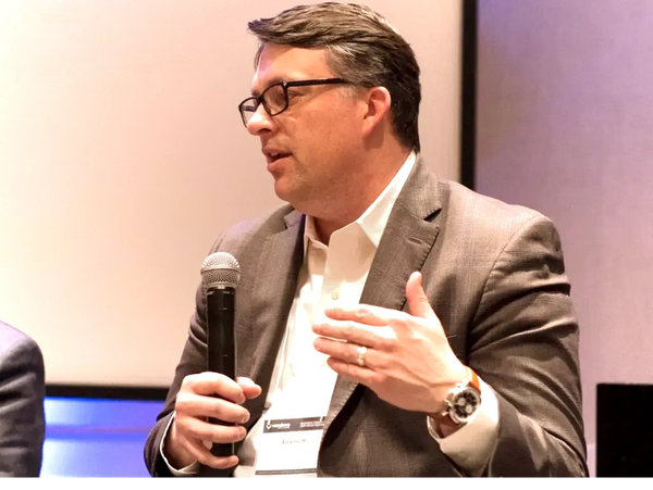 Man in glasses and suit speaking into a microphone during an event.