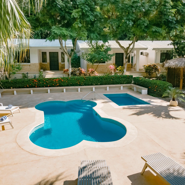 A uniquely shaped outdoor pool with lounge chairs and small cottages surrounded by greenery.