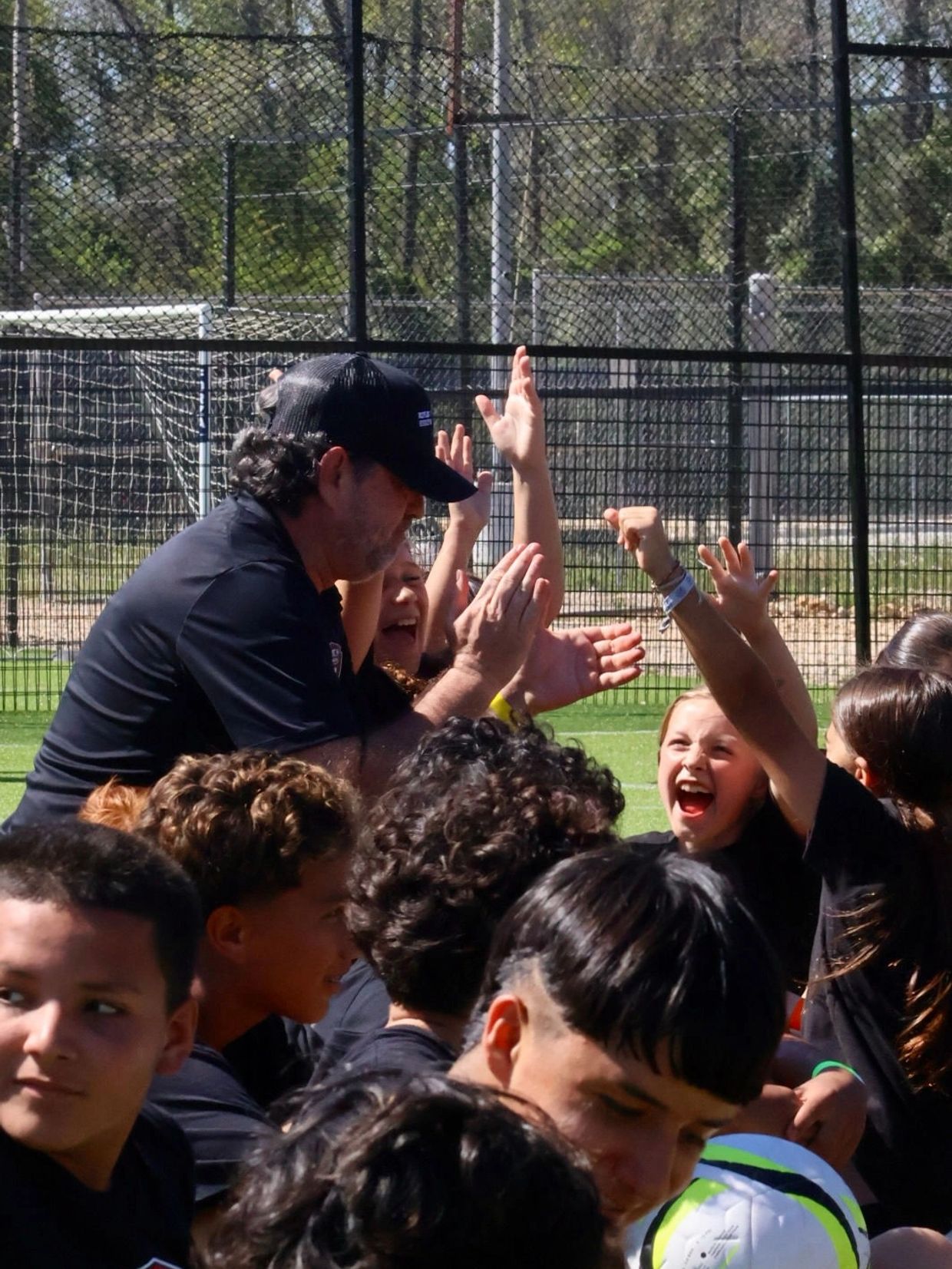 Coach and kids cheer excitedly on a soccer field, celebrating together.