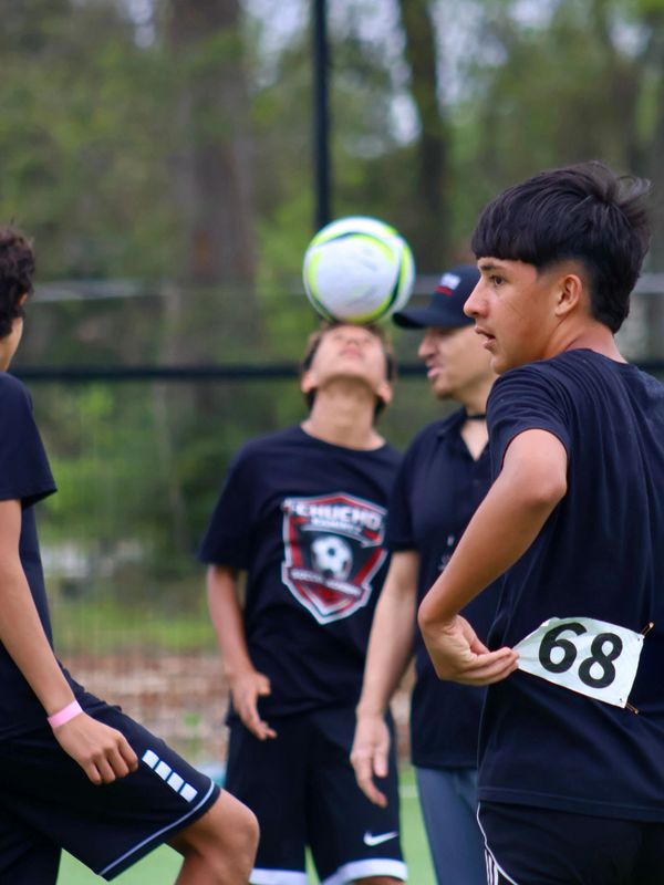 Teen soccer players practice, one balancing the ball on his head.