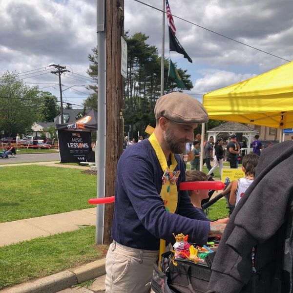 Man making balloon animals at an outdoor event.