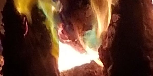 Close up of campfire at night with thick branches and multiple colors from powder additive