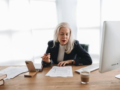 Older woman working at desk with papers and smartphone.