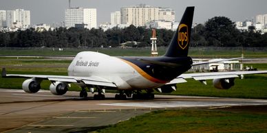 UPS cargo plane taxiing on an airport runway with cityscape in the background.