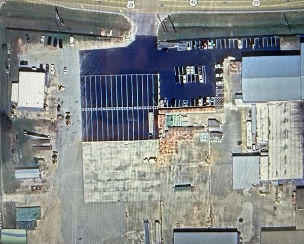 Aerial view of a parking lot and industrial buildings near a highway.