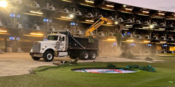 Excavator loading dirt into dump truck inside an indoor sports facility.