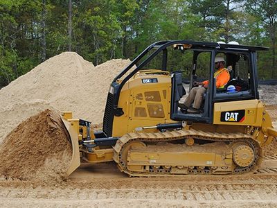 A construction worker operates a yellow CAT bulldozer moving sand.