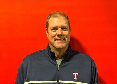 Man in a navy blue zip-up jacket standing against a bright red background.