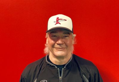 Man in a black jacket and white cap with a red logo stands against a red background.