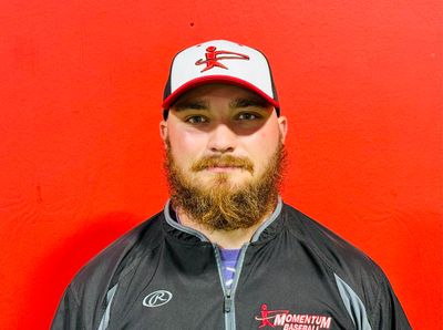 Man with beard wearing a baseball cap and jacket against a red background.