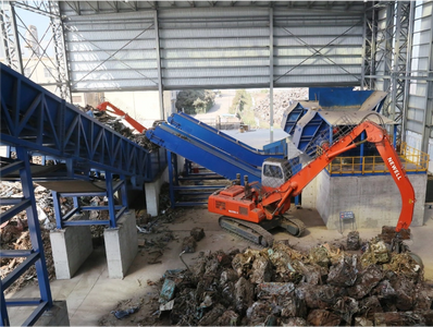 Industrial facility with conveyor belts and an orange excavator handling compacted waste.