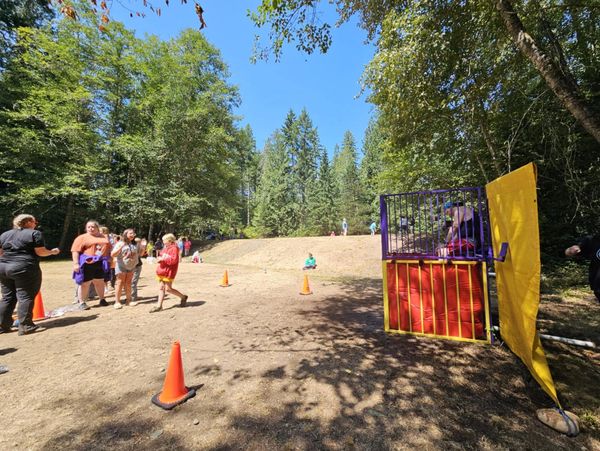Children and adults outdoors near a dunk tank on a sunny day.