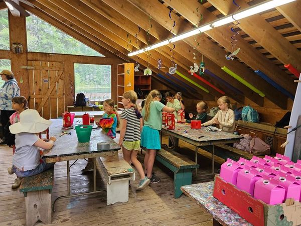 Children engaged in a craft activity inside a wooden cabin with colorful decorations.