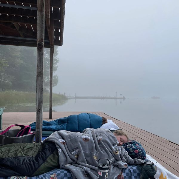 Two people sleeping on a dock by a foggy lake, wrapped in blankets.