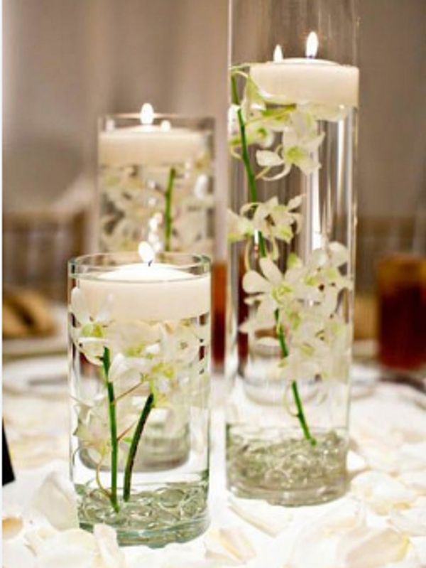 Elegant floating candles in tall glass vases with white flowers inside.