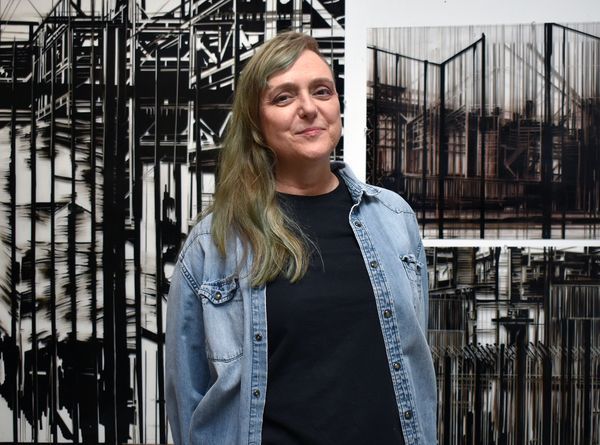 A woman stands smiling in front of abstract black and white artwork.
