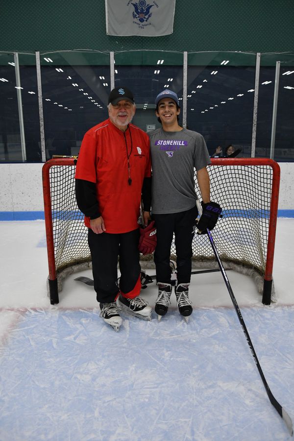 Two men posing on an ice hockey rink in front of a goal.