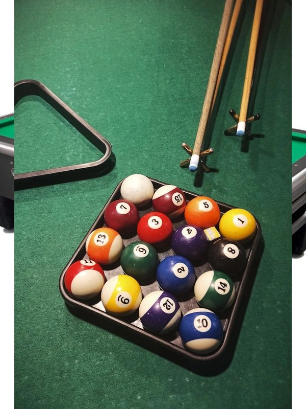 A rack of billiard balls, two cues, and a triangle on a green pool table.