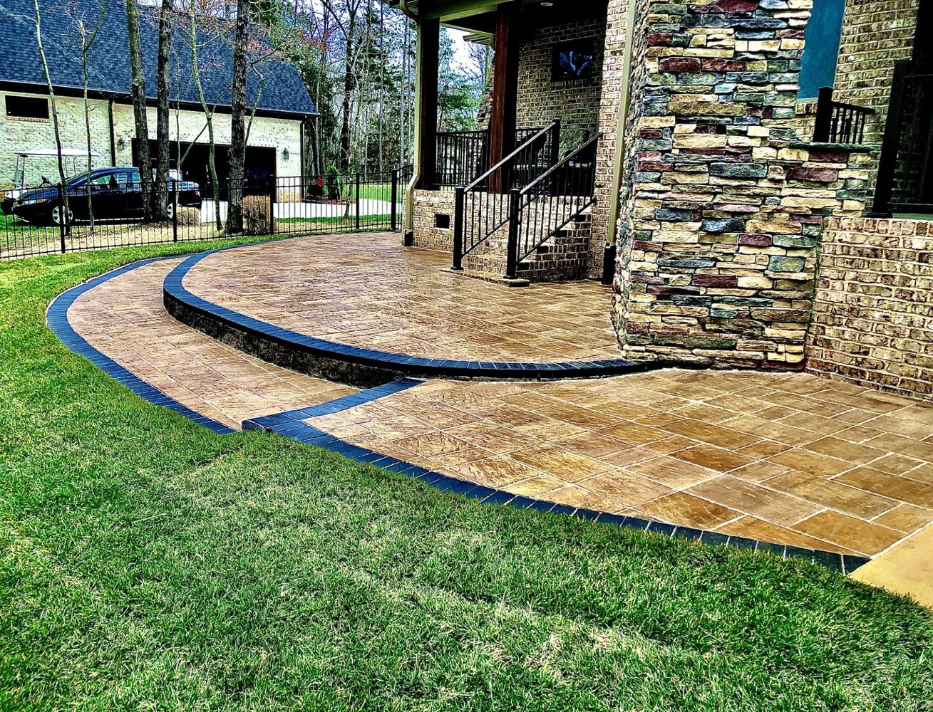 Elegant stamped concrete patio with stone wall and black railing.