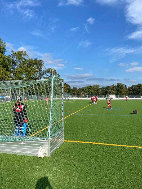 Young players practice field hockey on a sunny day at an outdoor sports field.