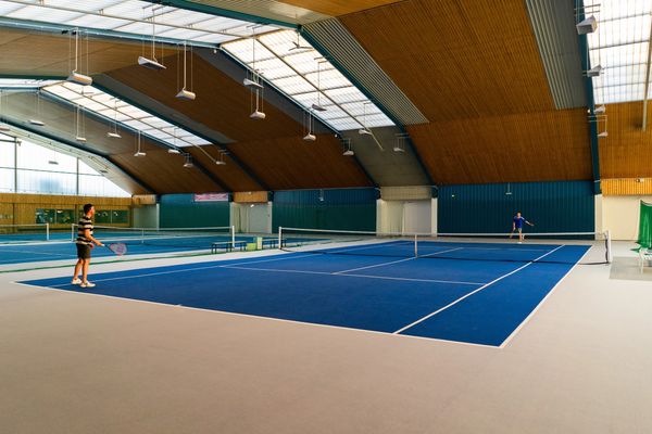 Two people playing tennis indoors on a blue court.