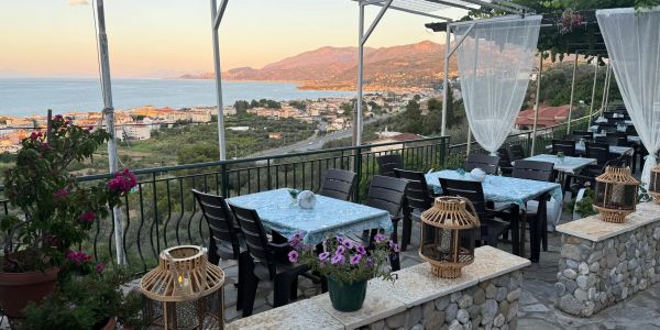 Outdoor dining area with sea and mountain view at sunset.