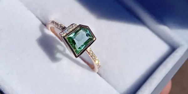 Elegant ring with a green gemstone and diamond accents on a gold band.