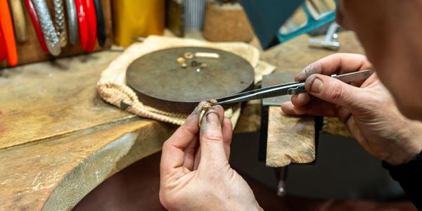 A jeweler using tweezers to inspect a ring on a workbench.