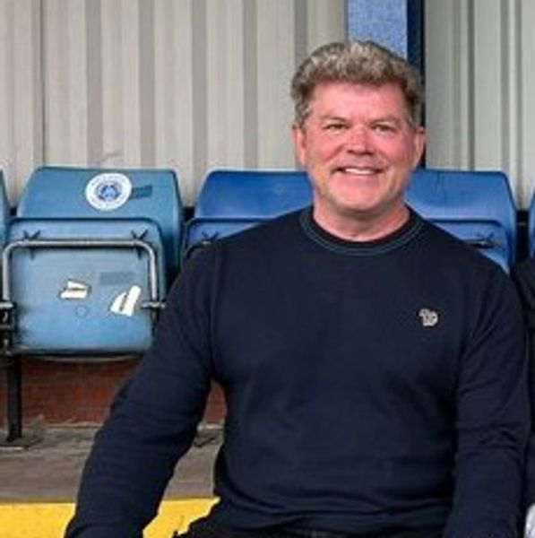 Smiling man in black sweater sitting on stadium seats.