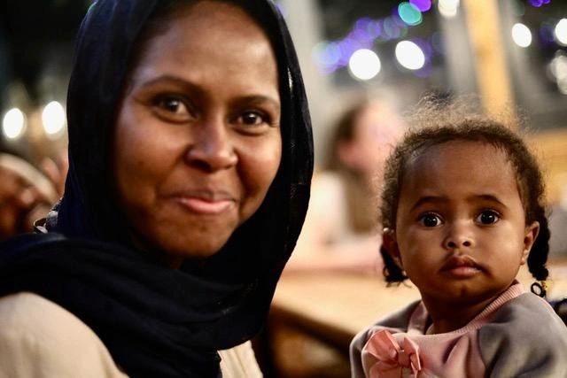 Smiling woman and curious child indoors.