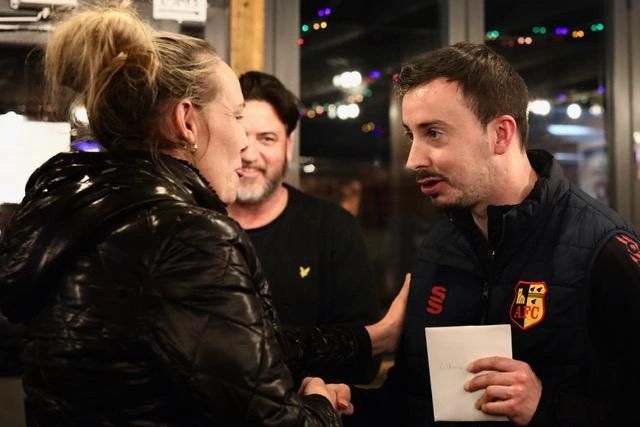 Three people engaged in a conversation indoors at night.