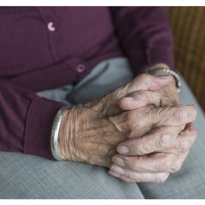 Close-up of elderly hands clasped together, showing wrinkles and a silver bracelet.
