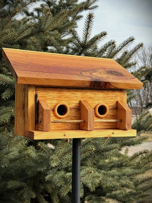 A handcrafted wooden birdhouse mounted on a black pole in front of pine trees.