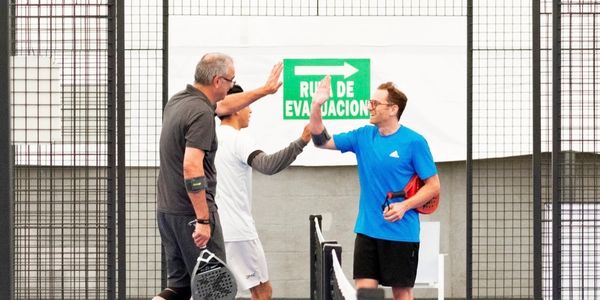 Three men in sportswear exchanging high-fives on a padel court.