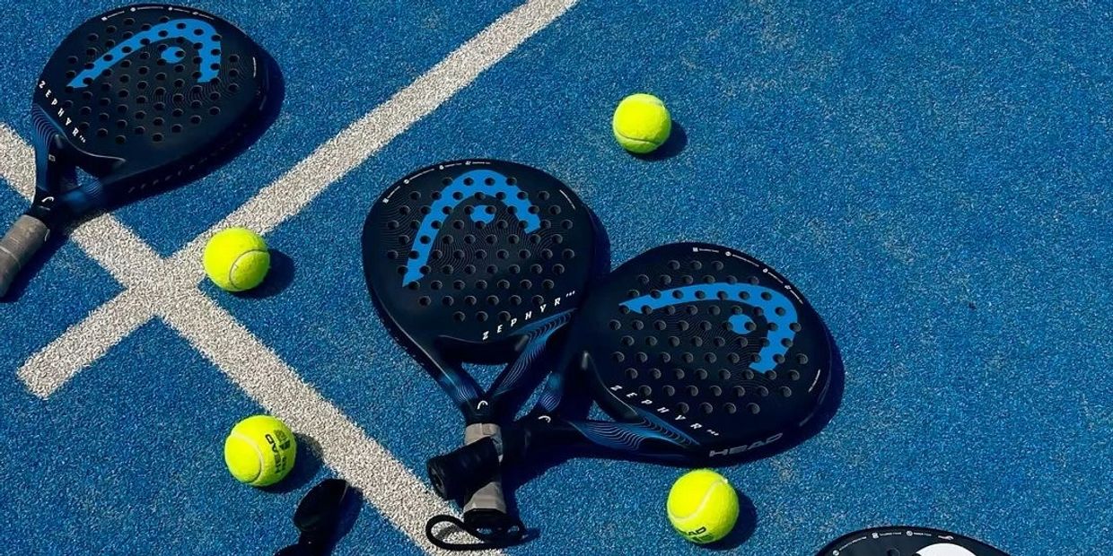 Padel rackets and tennis balls on a blue court.