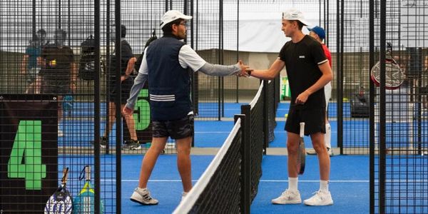 Two players shaking hands over the net on a blue padel court.