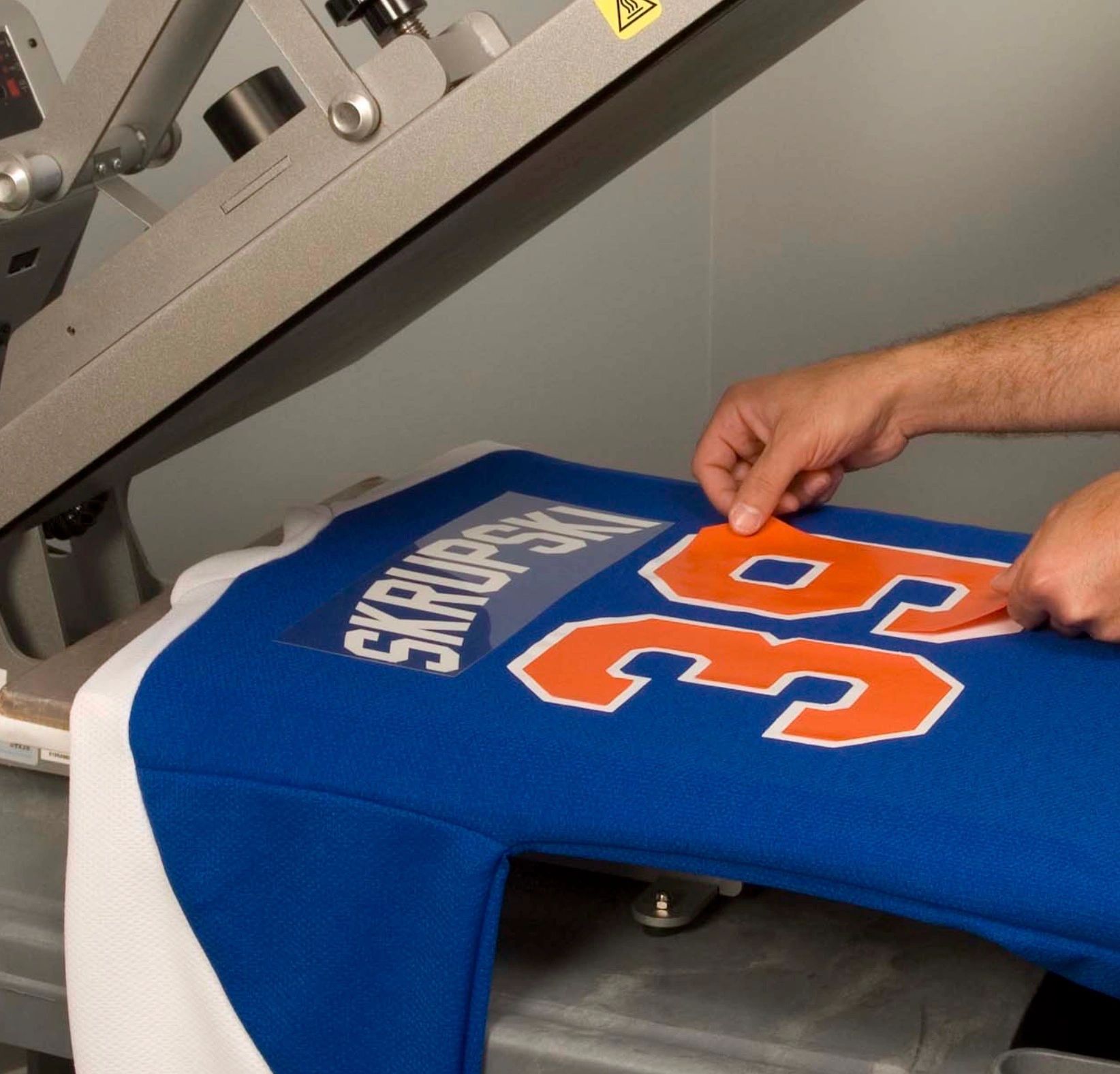 Hands applying number patches on a blue sports jersey.